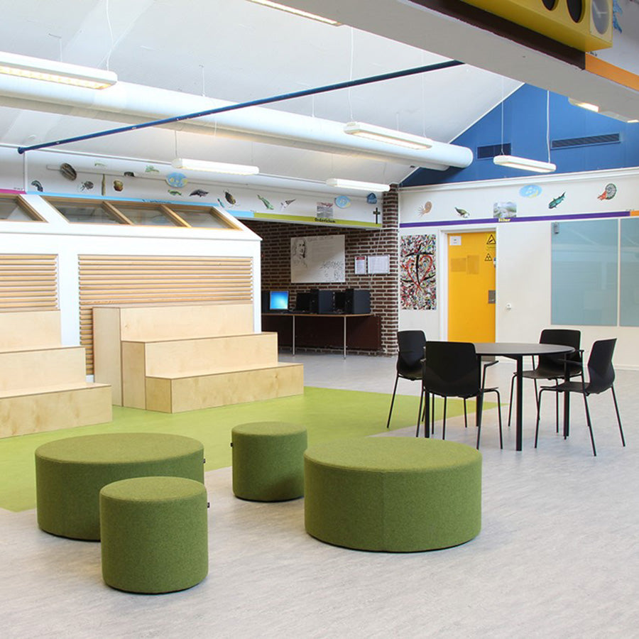Modern classroom with green round Point ottomans or stools, black chairs, and a table.