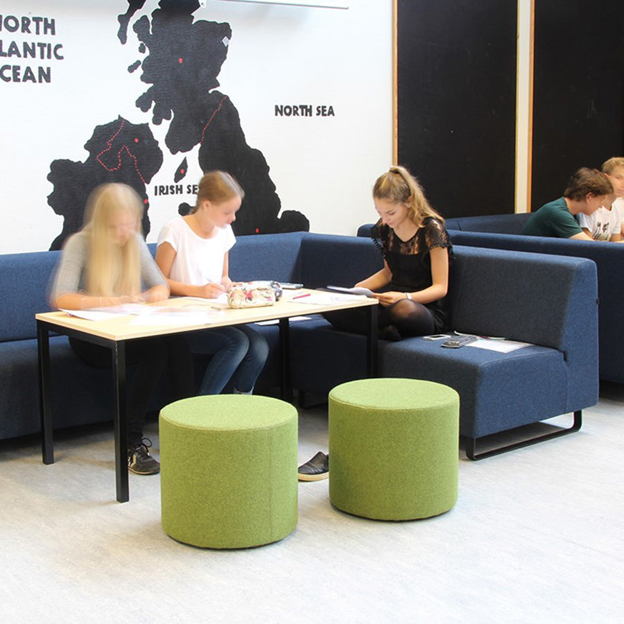 People sitting on blue couches around a table with green Point ottomans in a room with a world map on the wall.