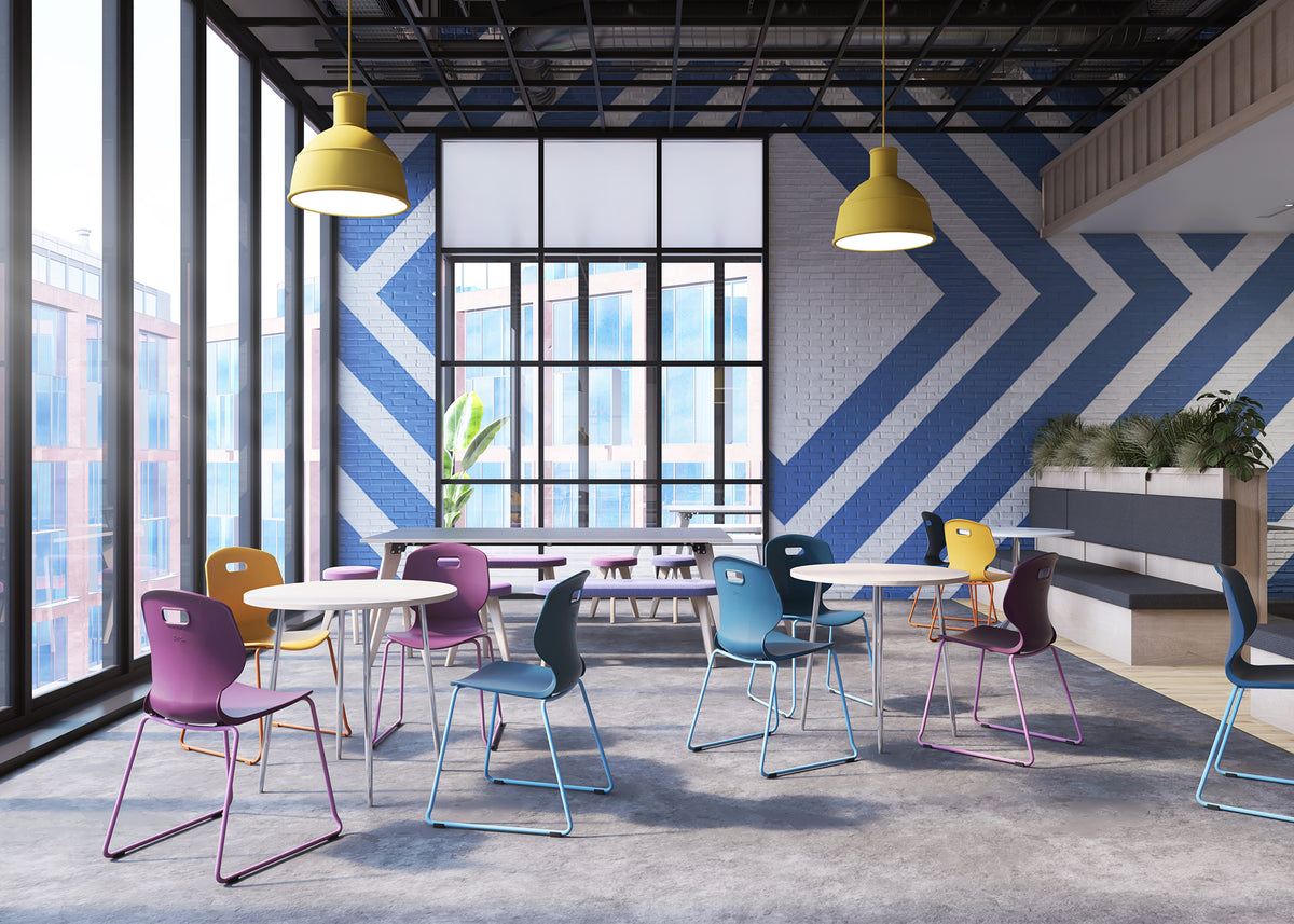 A modern interior space with colorful chairs and tables arranged around large windows. The room features bold blue and white geometric wall panels, yellow pendant lights, and a concrete floor.